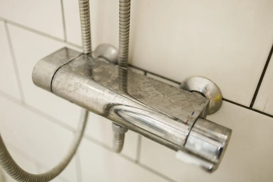 Close up of shower mixer faucet with limescale, white chalky deposit and stains Formed on the plumbing system by a combination of soap residues and hard water Concept of cleaning limescale plumbing