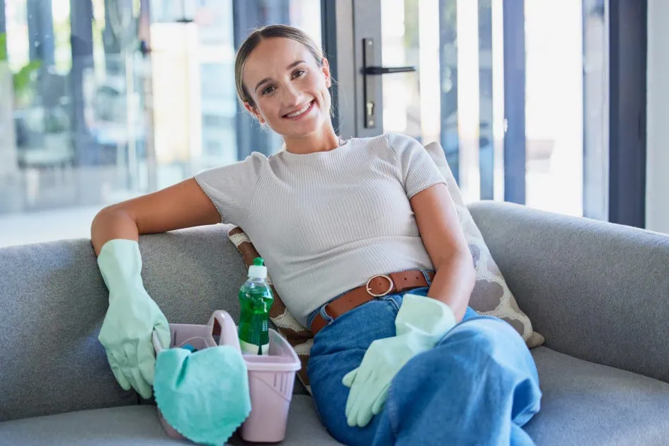 cleaning lady sitting on sofa with cleaning supplies