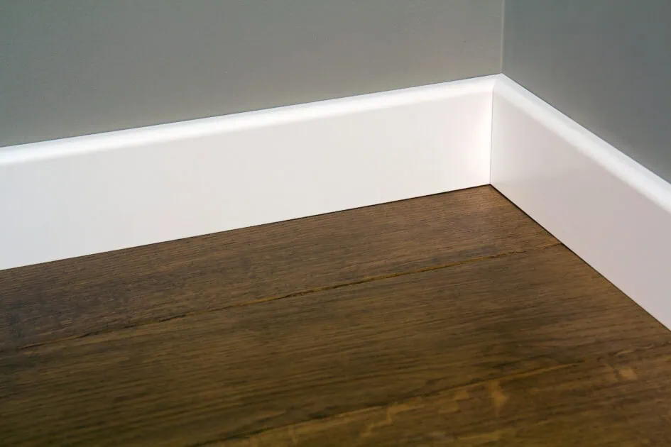 Clean white baseboards on a wood floor after thorough dusting and wiping.