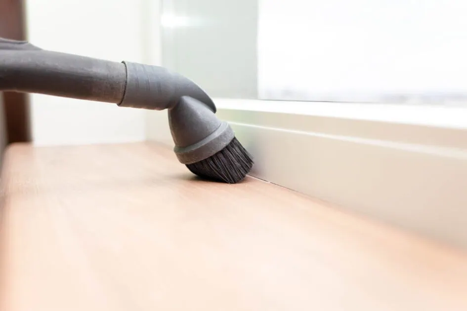Vacuuming baseboards with a brush attachment to remove built-up dust and dirt.