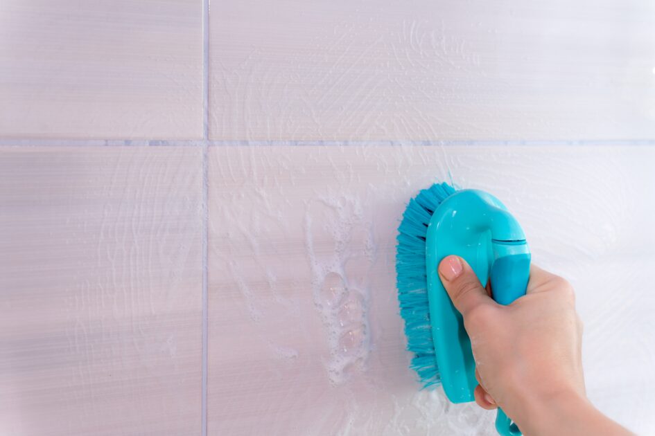 a cropped hand washes a tile in bathroom